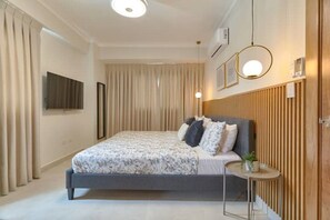 A modern bedroom with a large bed, a small bedside table, and a TV mounted on the wall.