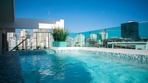 A rooftop swimming pool with a cityscape view, a staircase leading to the pool, and a potted plant.