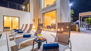 A rooftop lounge area with sun loungers, a table with drinks, and a view of the interior of the building.