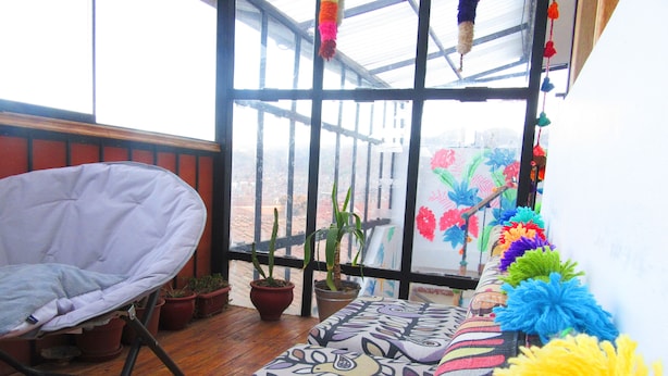 A room with a white chair, a patterned rug, potted plants, and a view through a large window. - COMFORTABLE & COZY HOUSE IN SAN BLAS (Cusco)