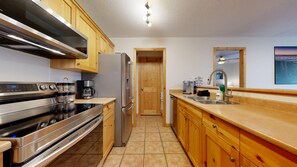 A modern kitchen with stainless steel appliances, wooden cabinets, a built-in oven, and a sink. - Crystal Forest #31 | 3 Peaks Rentals (Sun Peaks)