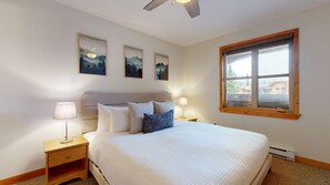 Un dormitorio con una cama, dos mesitas de noche, un ventanal y tres cuadros colgados en la pared.