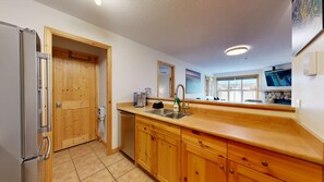 A kitchen with wooden cabinets, a stainless steel sink, and a refrigerator. - Crystal Forest #31 | 3 Peaks Rentals (Sun Peaks)