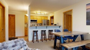 A compact kitchen with wooden cabinets, a central island with stools, and a dining table with chairs.