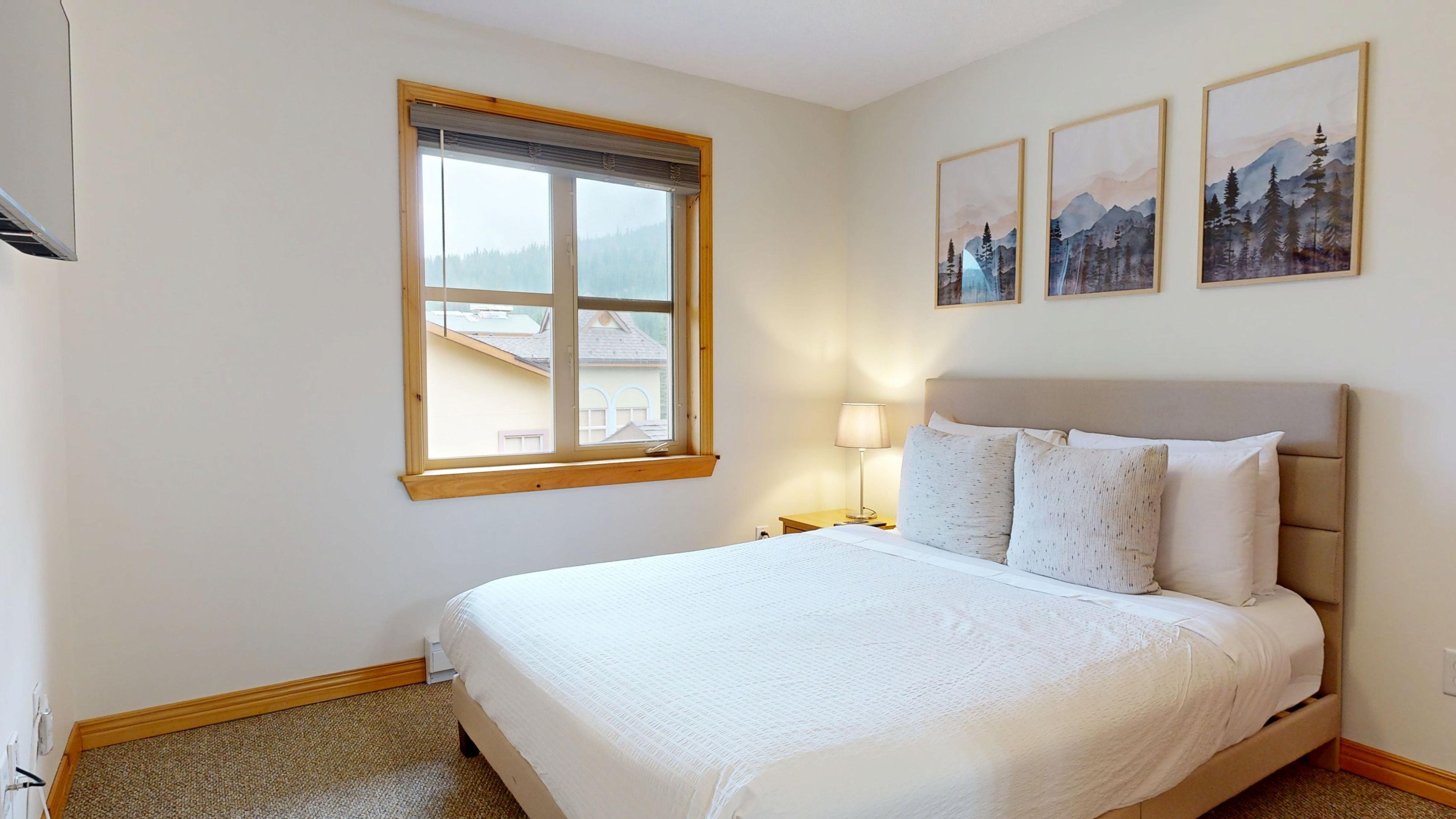 A bedroom with a large bed, a window with a view, and two framed pictures on the wall.