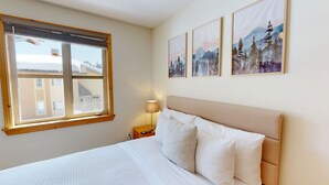 A bedroom with a bed, a nightstand, a lamp, and three framed pictures on the wall. - Welcome to Cozy at the Crystal (Sun Peaks)
