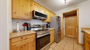 Una cocina con armarios de madera, electrodomésticos de acero inoxidable y piso de baldosas.
