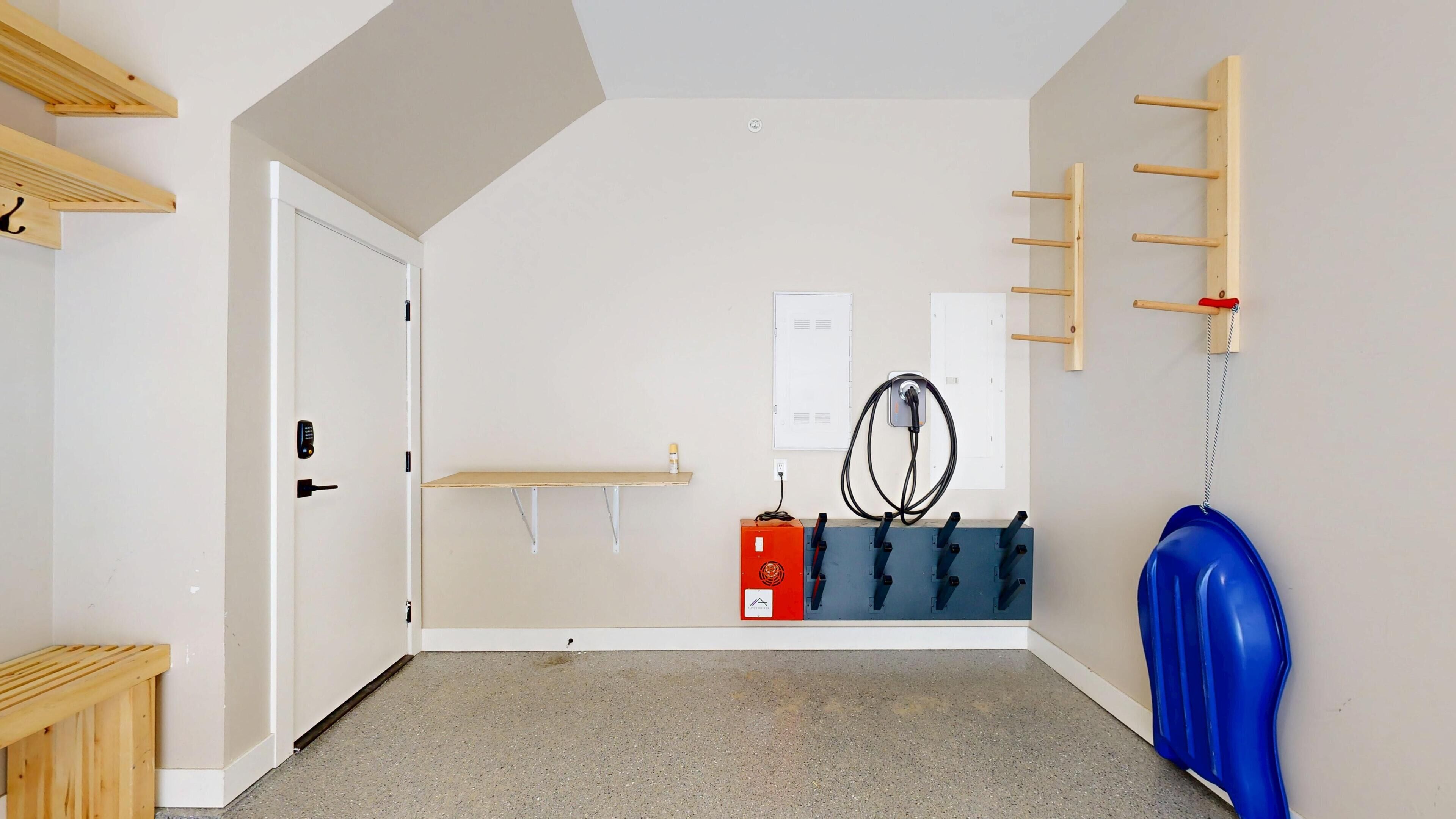 Una habitació amb una porta, una estant, una presa elèctrica, una caixa elèctrica vermella, un compressor d'aire blau i una prestatgeria penjada a la paret.