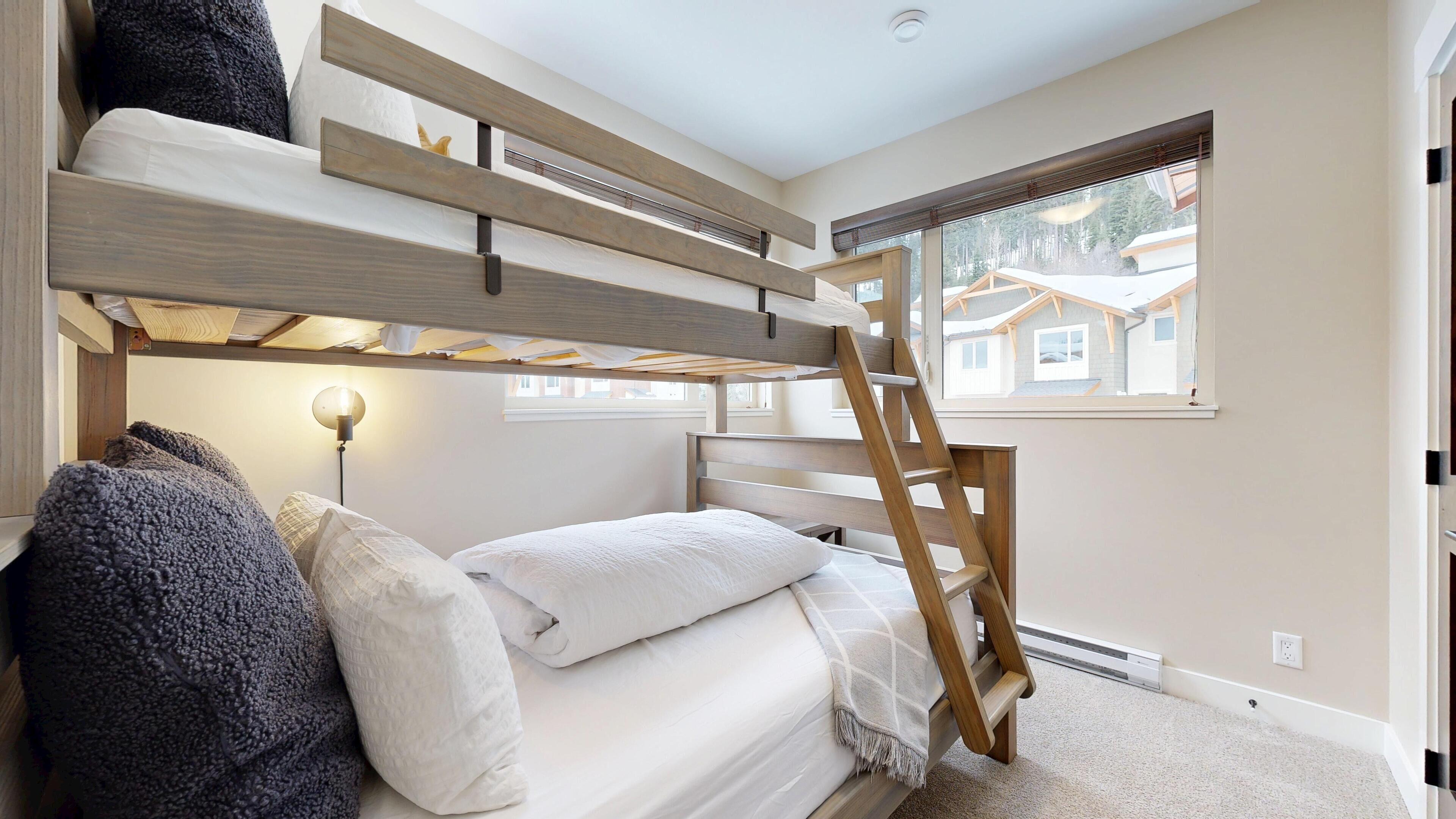 Une chambre avec un lit superposé, une échelle, une lampe et une fenêtre donnant sur des maisons.