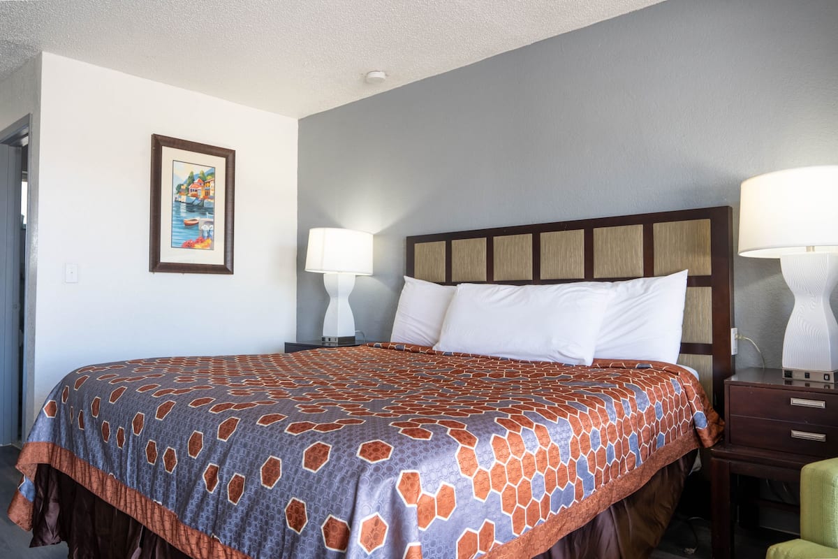 A hotel room with a large bed, two bedside lamps, a nightstand, and a framed picture on the wall.