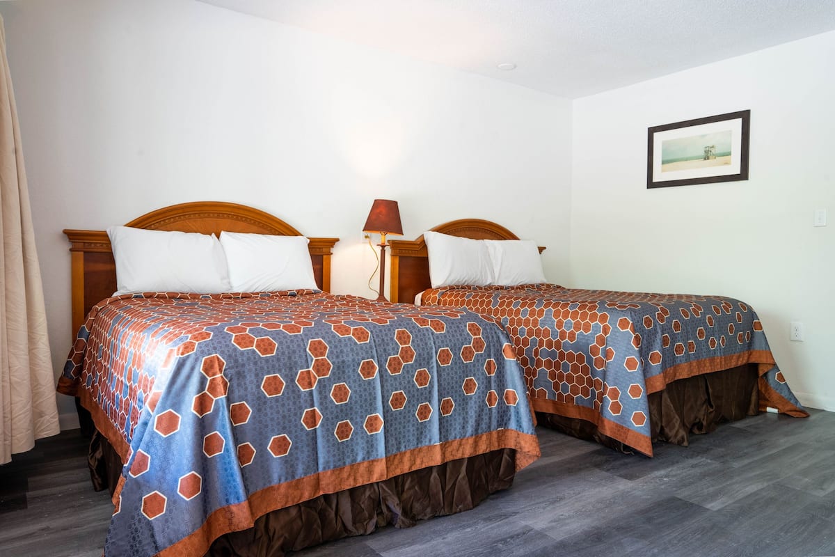 A hotel room with two beds, each with a wooden headboard, a nightstand, and a lamp.
