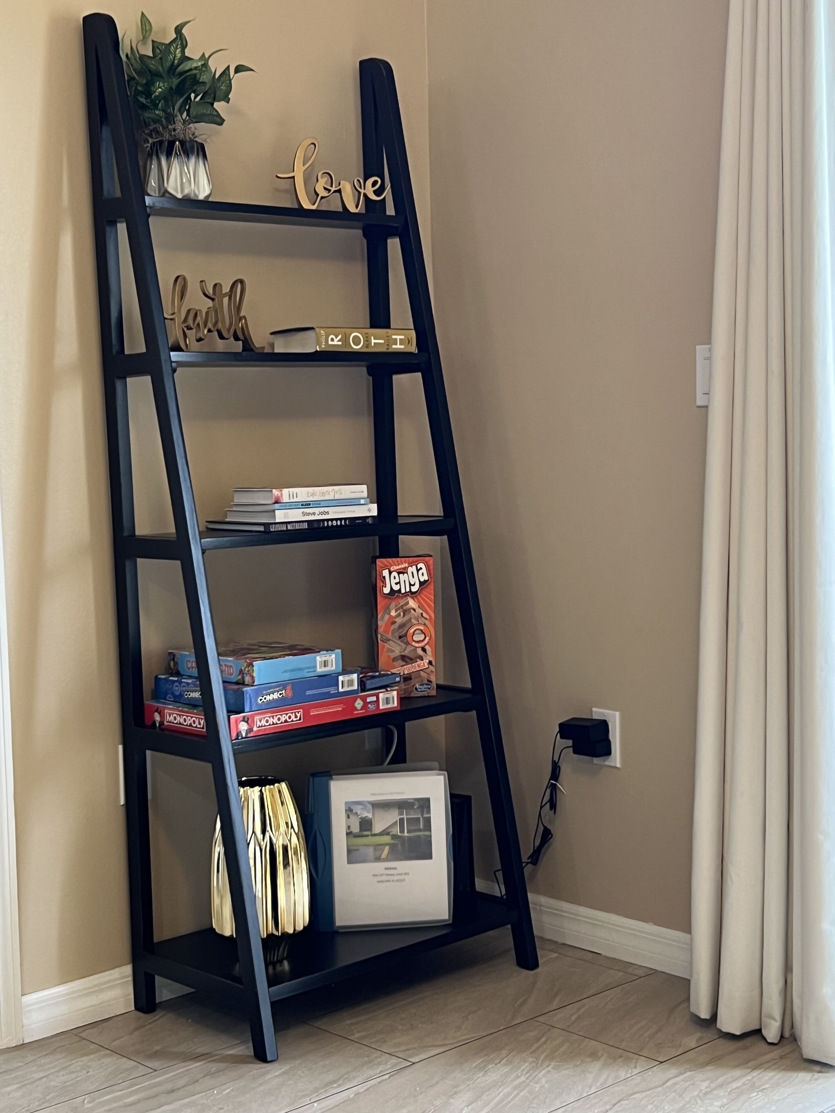 Eine schwarze Bücherwand mit Büchern, Gesellschaftsspielen und Dekoration vor einer beige farbenen Wand.