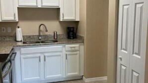 A kitchen with white cabinets, a sink, and a coffee maker. - Peace and Quiet near Daytona (Holly Hill)