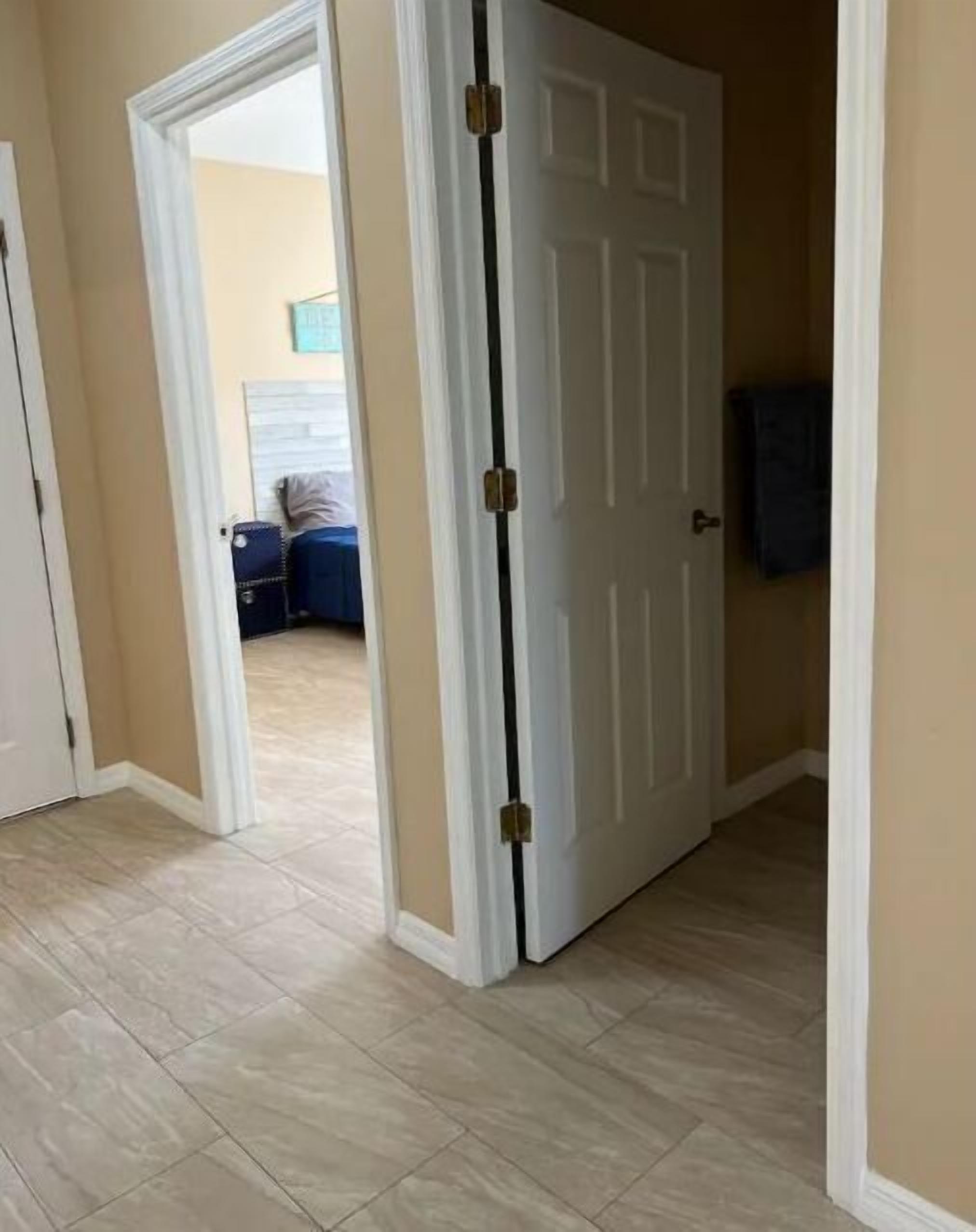 Un corridoio con una porta bianca, pareti beige e pavimento piastrellato.