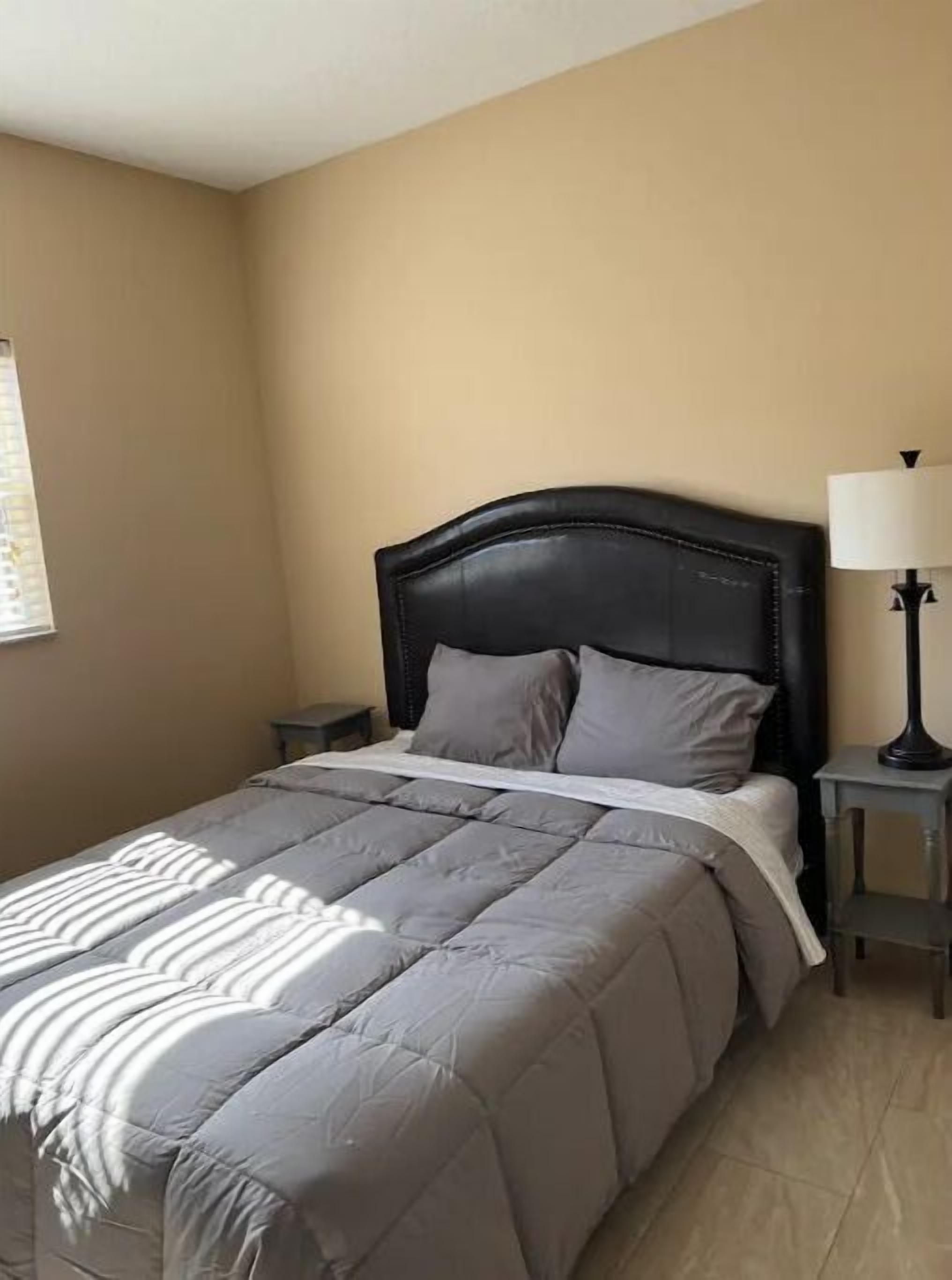 A bedroom with a bed, a nightstand, a lamp, and a window with blinds.