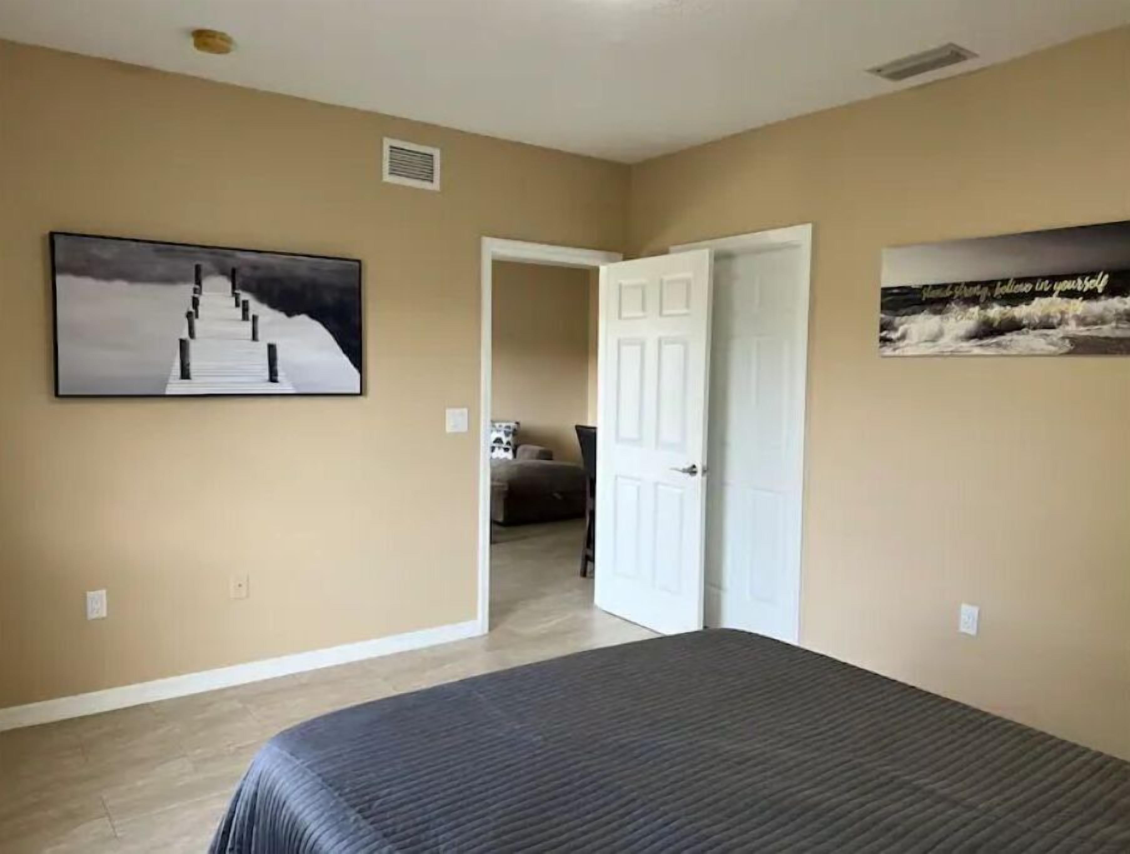 A bedroom with a bed, a door leading to another room, and two wall-mounted pictures.
