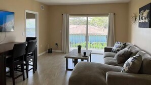 A living room with a sofa, a coffee table, and a TV. There is a balcony with a view of a fence and trees. - Peace and Quiet near Daytona (Holly Hill)