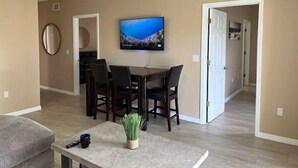 A dining area with a TV mounted on the wall, a dining table with chairs, and a small plant on a table. - Peace and Quiet near Daytona (Holly Hill)