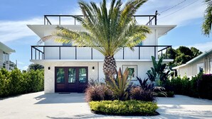 Ein modernes, zweistöckiges Haus mit breitem Auffahrt, einer Palme und verschiedenen Pflanzen.