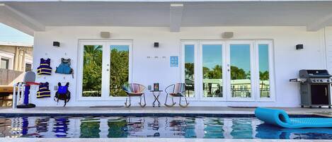 Ein modernes, zweistöckiges Haus mit Swimmingpool, Sitzgelegenheiten im Freien und Grill.