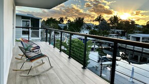 Ein Balkon mit Schaukelstuhl, Blick auf den Sonnenuntergang und ein Yachthafen mit Booten.
