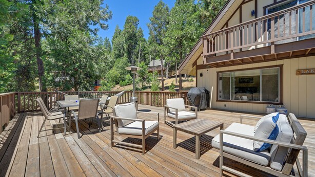 A wooden deck with outdoor furniture, including chairs and a table, overlooking a forested area.