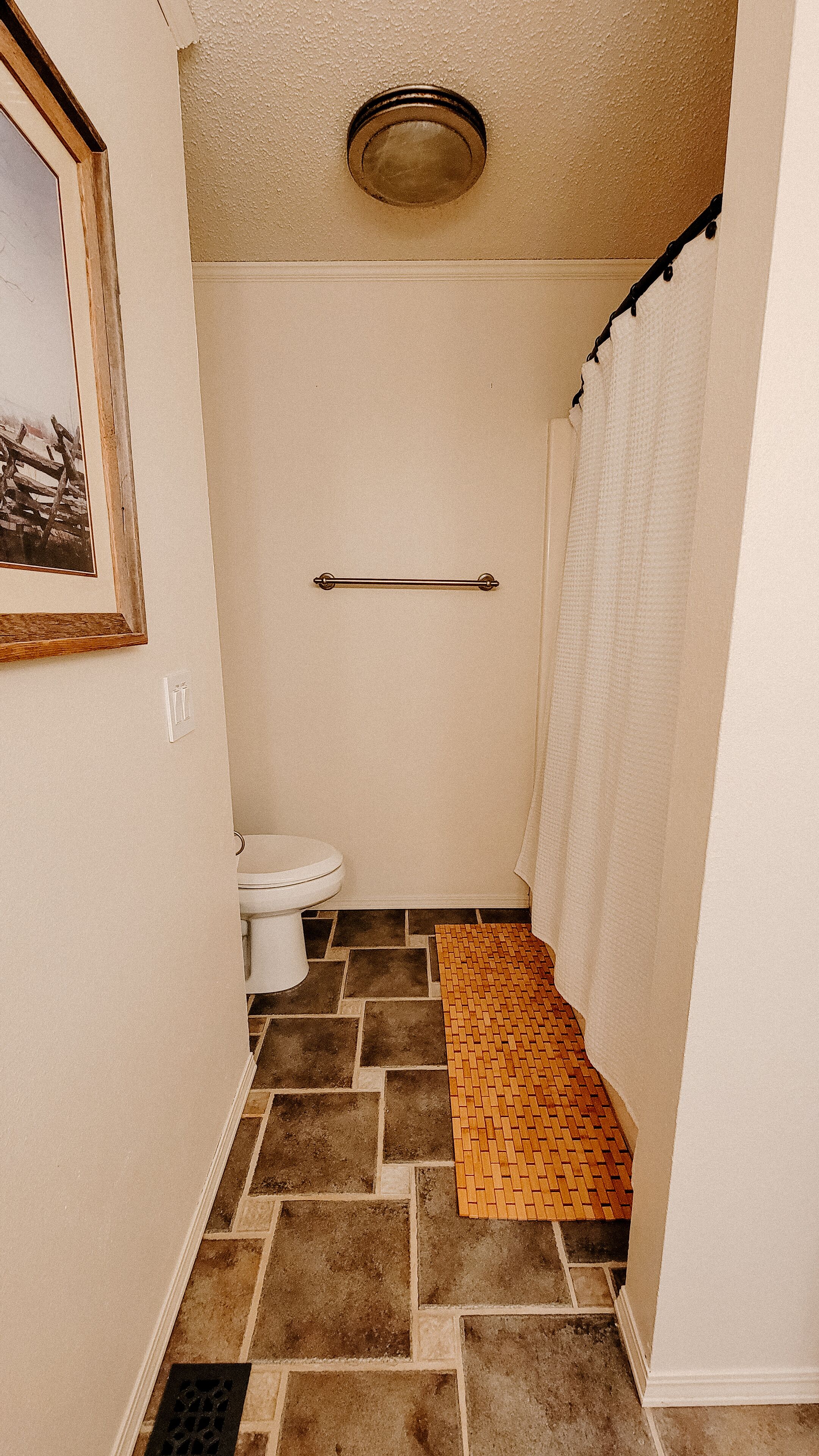 A small, narrow bathroom with a toilet, a towel rack, and a shower curtain.