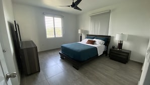 A bedroom with a bed, a nightstand, a lamp, a ceiling fan, a window, and a door. - Casa Orillia's Del Mar / 7 minutes from Jobo's Beach  (Isabela)