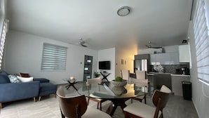 A modern living room with a blue sofa, a glass dining table, and a kitchen area with a refrigerator and microwave. - Casa Orillia's Del Mar / 7 minutes from Jobo's Beach  (Isabela)