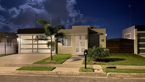 A modern two-story house with a garage, a small front yard, and a street view at night. - Casa Orillia's Del Mar / 7 minutes from Jobo's Beach  (Isabela)