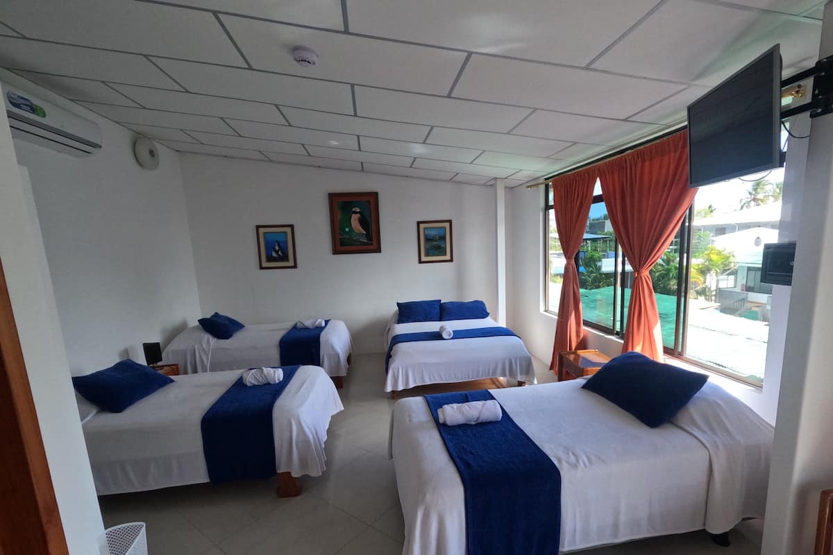 Ein Hotelzimmer mit vier Einzelbetten, einem Deckenventilator, einer Klimaanlage und einem Fernseher.