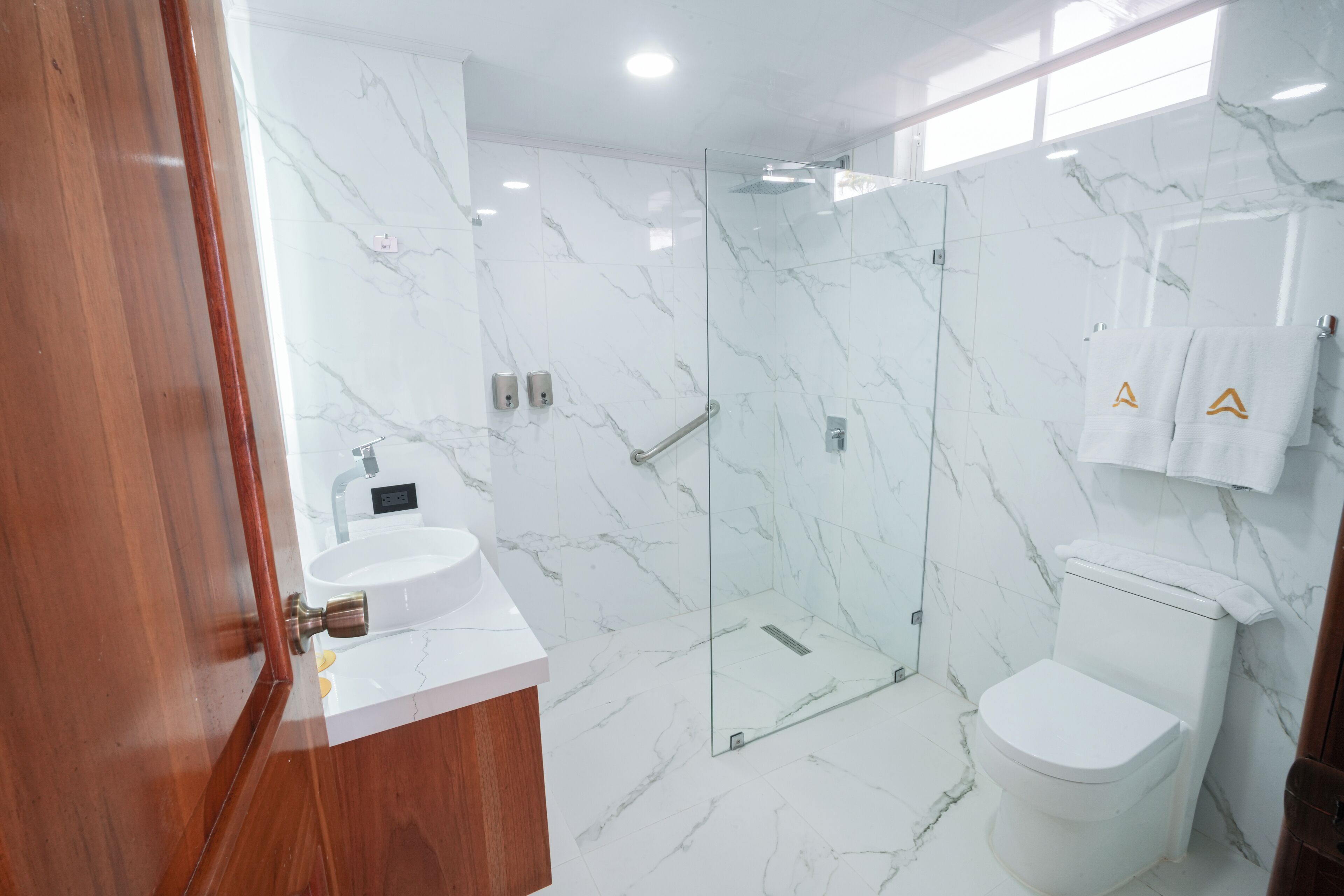 Un baño moderno con piso de mármol, cabina de ducha de vidrio, lavamanos blanco y un inodoro.