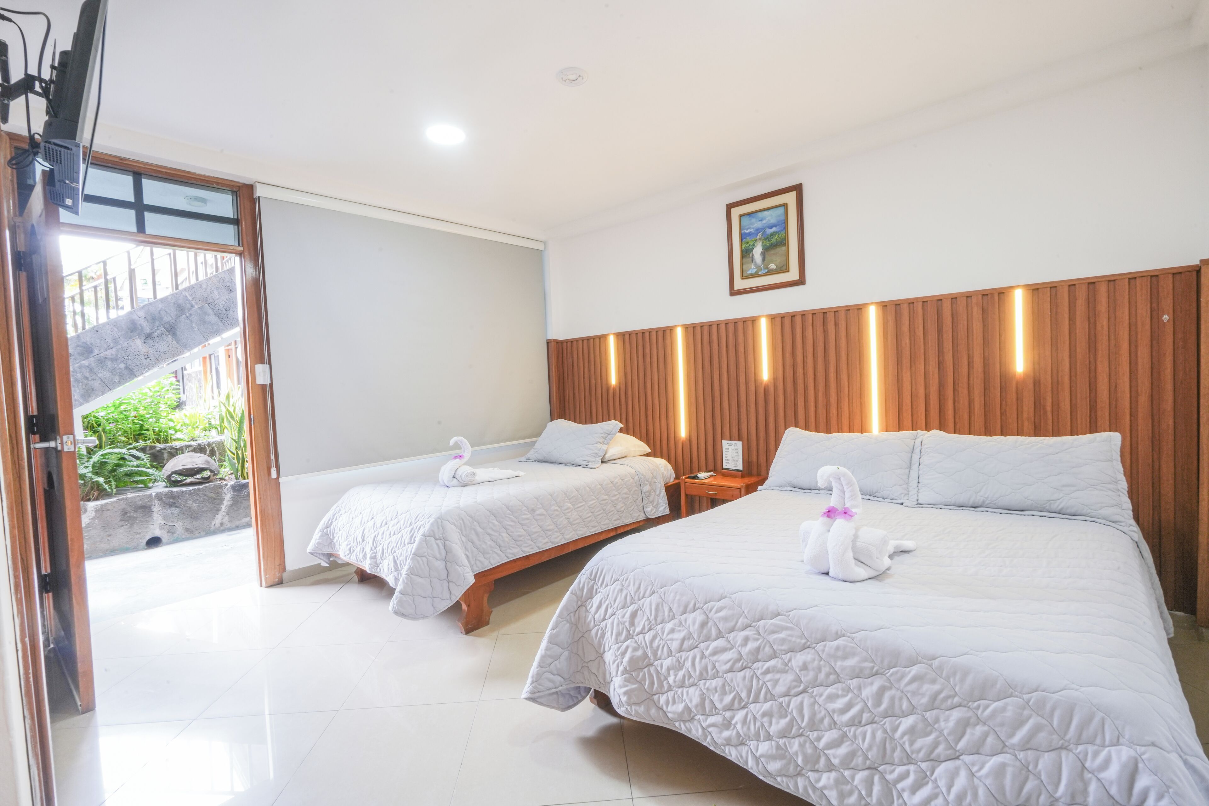 A hotel room with two beds, each with a swan-shaped pillow, a wooden headboard, and a small bedside table.
