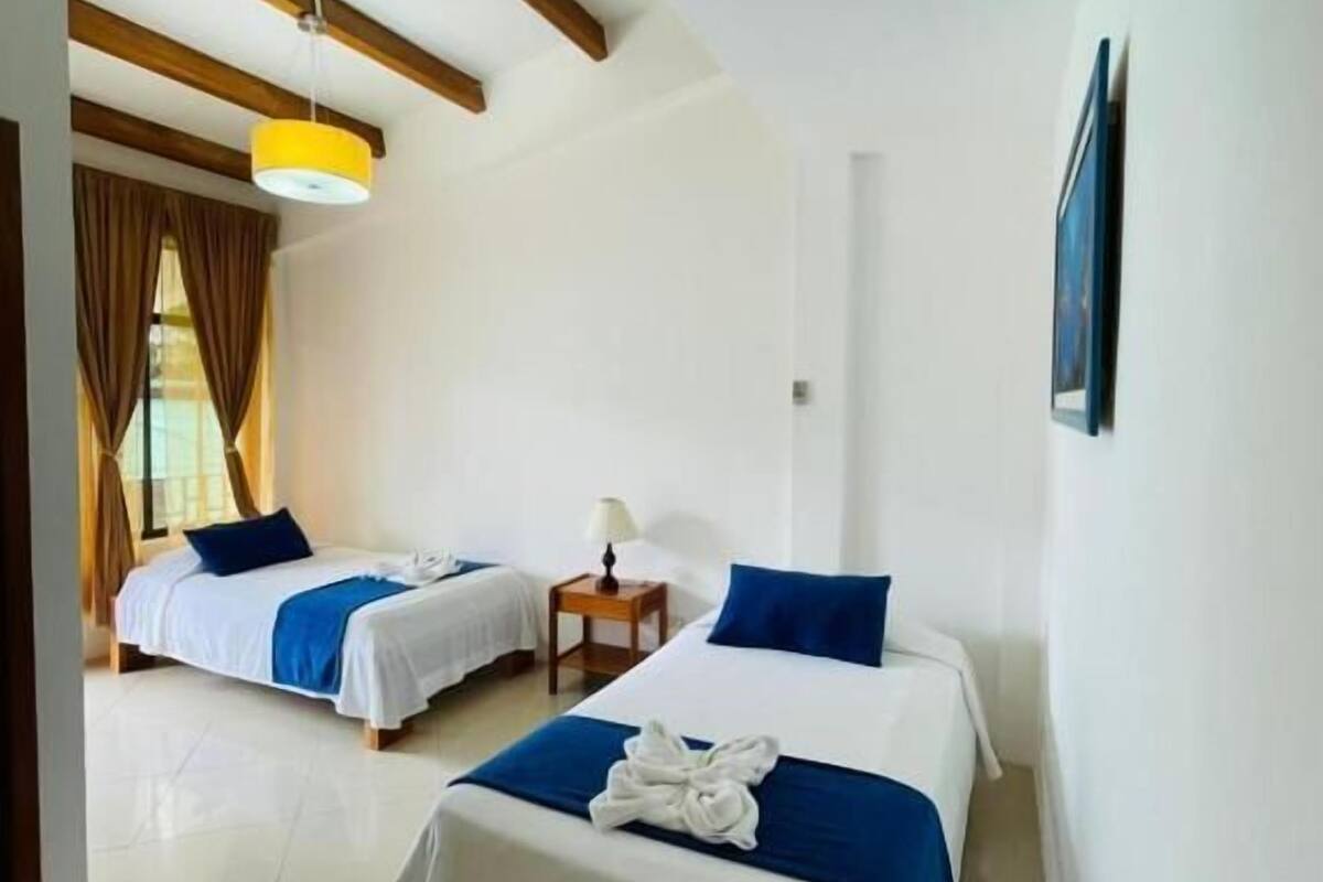 Ein Hotelzimmer mit zwei Betten, einer Holzbalkendecke und einem kleinen Tisch mit einer Lampe.