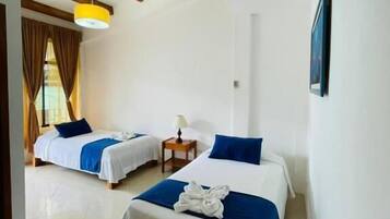 A hotel room with two beds, a wooden ceiling, and a small table with a lamp.
