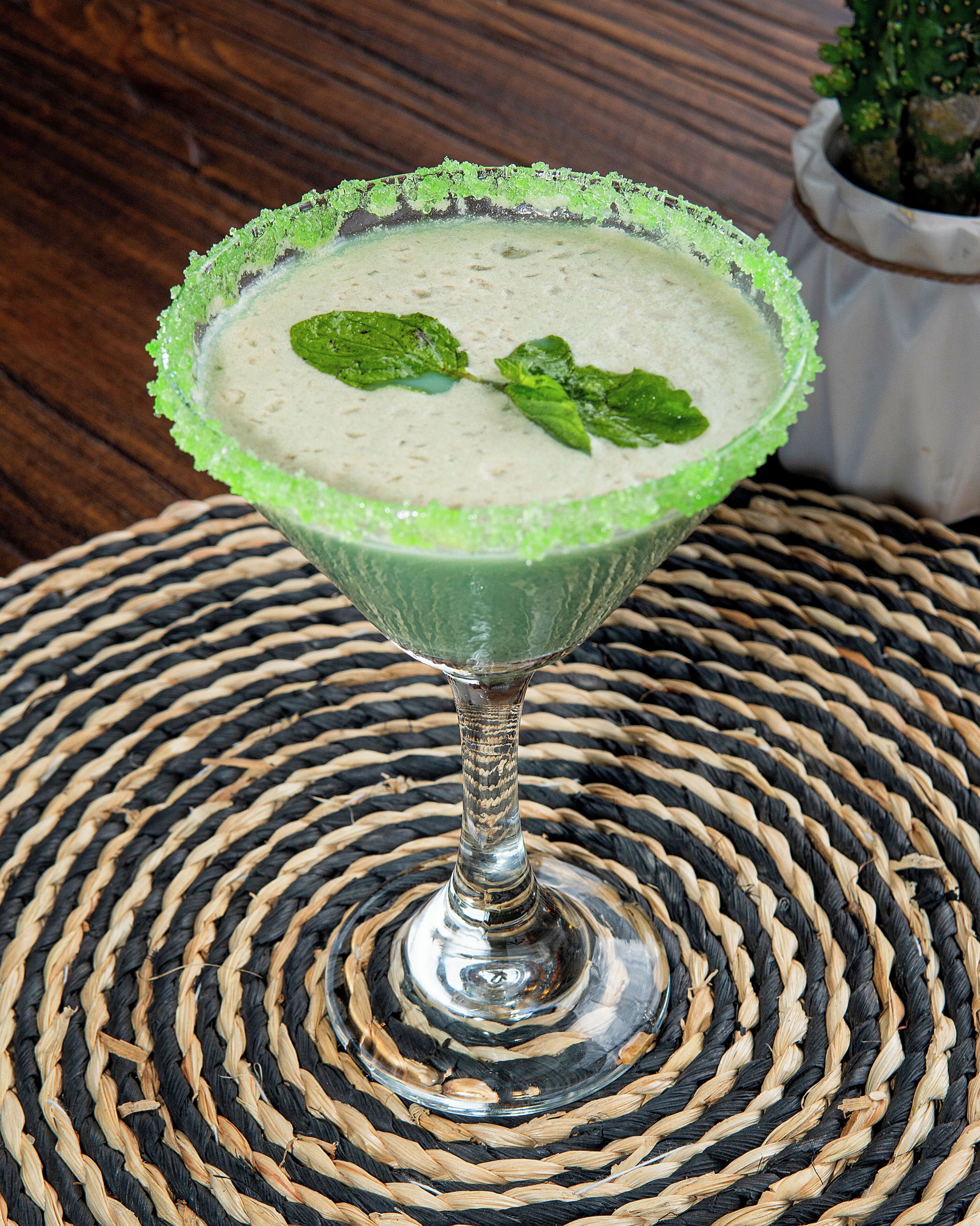 Un cocktail servi dans un verre dont le bord est vert, posé sur un tapis tressé.