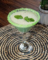 Un cocktail servi dans un verre dont le bord est vert, posé sur un tapis tressé.