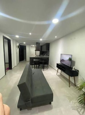 A modern living room with a sofa, a TV, and a kitchen area in the background.