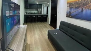 Een moderne woonkamer met een flatscreen televisie, een zwarte bank en een stadslandschap schilderij aan de muur.