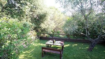Une table en bois avec un banc, le tout installé dans un jardin luxuriant.
