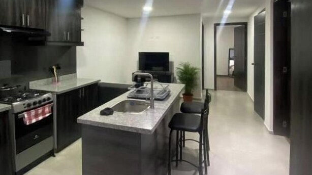 A modern kitchen with a central island, dark cabinetry, and a flat-screen TV.