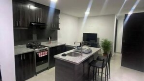 A modern kitchen with dark cabinetry, a central island with bar stools, and a built-in oven.