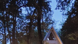 A cabin with a wooden staircase leading up to a deck, surrounded by trees.