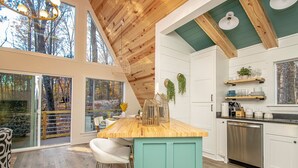 A modern kitchen with a wooden island, white cabinetry, and a view of the forest through large windows.