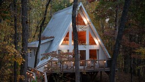 A cabin with a steeply pitched roof, wooden deck, and a staircase leading to the entrance.
