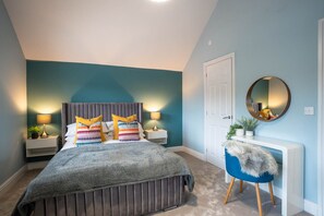 A bedroom with a bed, bedside tables, a chair, a mirror, and a door. - All Saints (Worcester)