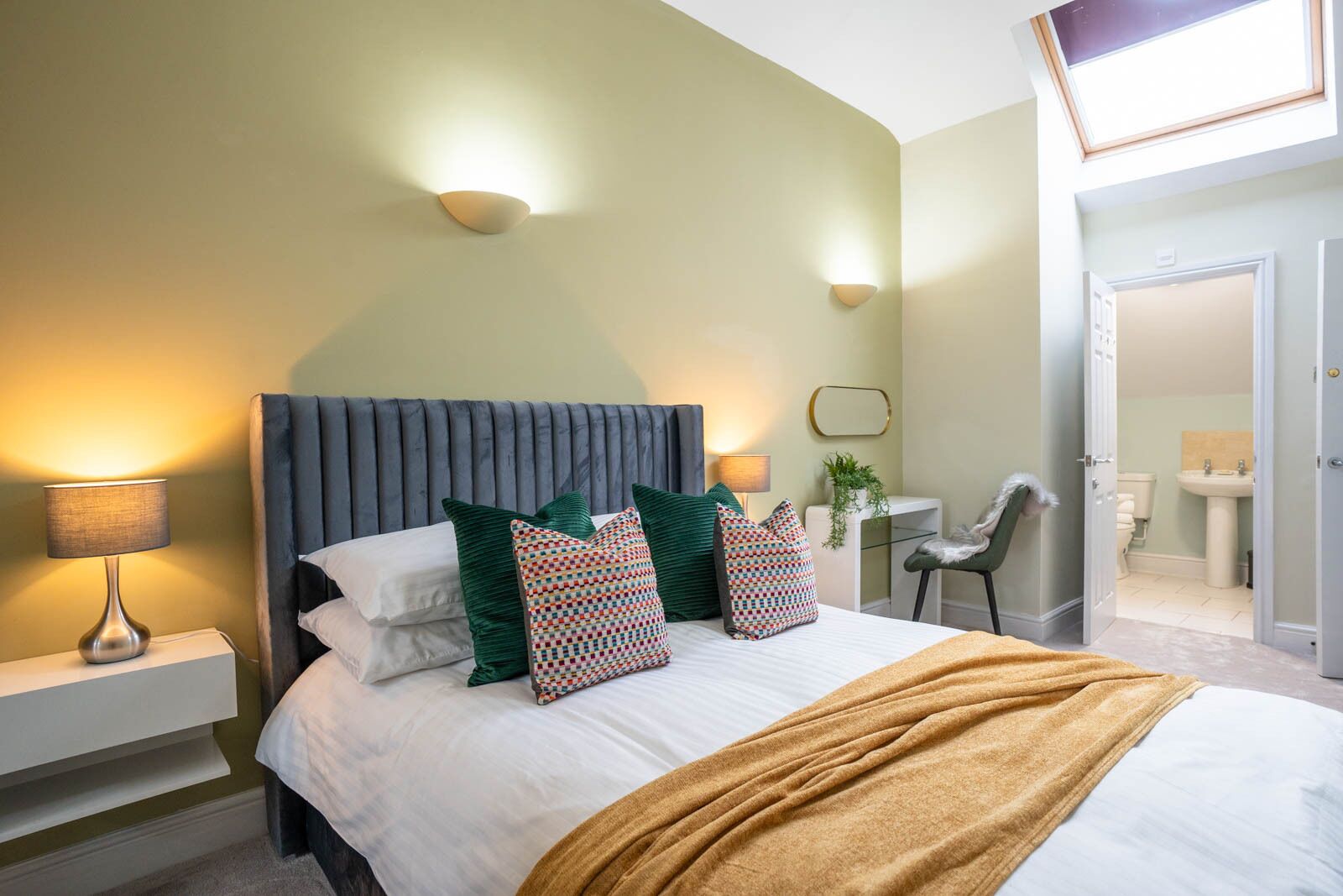 Un dormitorio moderno con una cama grande, dos lámparas de noche, una silla y vistas al baño.
