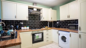 Una cocina con gabinetes blancos, salpicadero de baldosas negras, estufa, microondas y lavadora.
