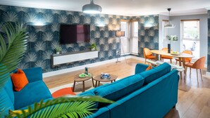 Una sala de estar moderna con un sofá color turquesa, un televisor de pantalla plana y una zona de comedor con sillas naranjas.