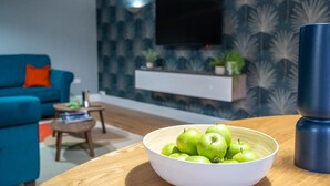 Una sala de estar moderna con un sofá azul, una mesa de centro de madera y un cuenco de manzanas verdes.